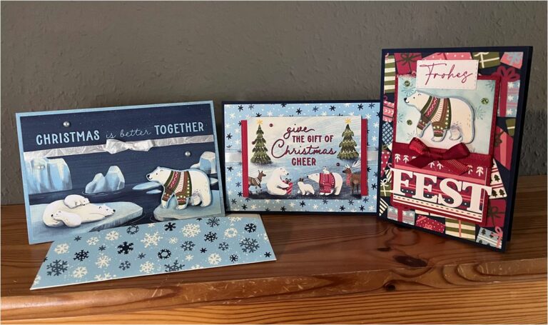 Auf einem rustikalen Holztisch liegen drei Weihnachtskarten mit festlichen Motiven und fröhlichen Botschaften.