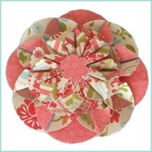 Ein mehrlagiges, kreisförmiges Papierblüten-Ornament, mit roten und gemusterten Abschnitten mit floralen und geometrischen Designs, weckt charmante Retro-Impressionen.