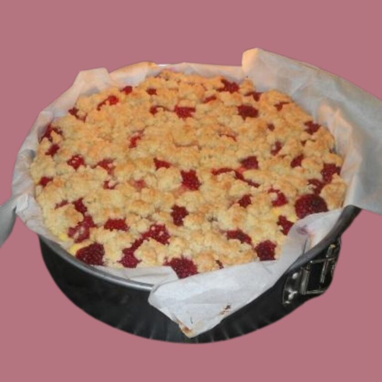 mit goldbrauner Kruste und köstlicher roter Fruchtfüllung, das an eine Himbeer-Käsetorte erinnert, mit Backpapier ausgelegt in einer runden Backform vor rosa Hintergrund.