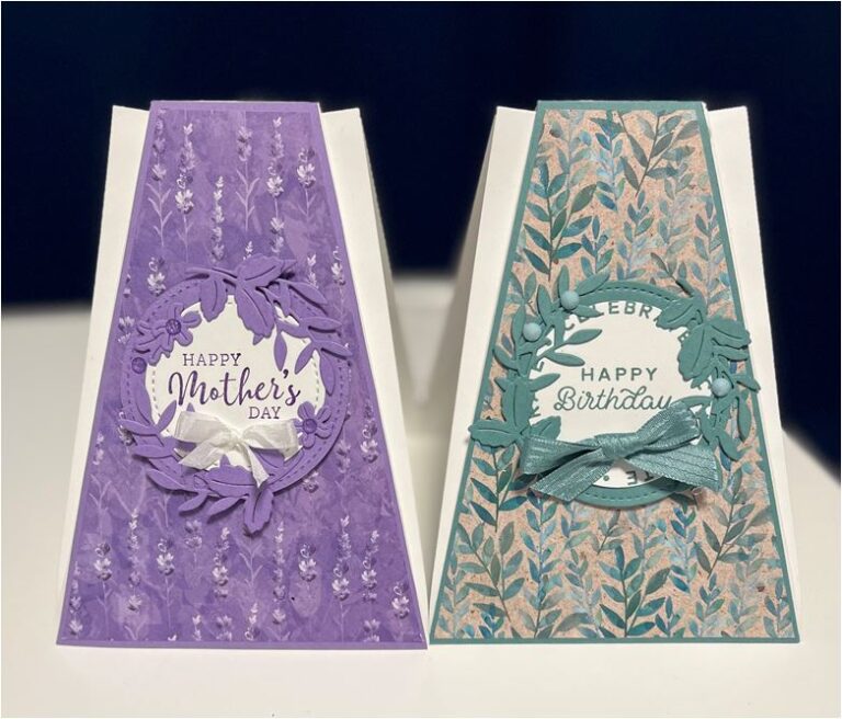 Zwei handgemachte Grußkarten, die aufrecht auf einem Tisch ausgestellt sind, eine feiert den Muttertag mit violetten Blumenmustern und die andere einen Geburtstag mit grünen „Mach was draus“-Designs.