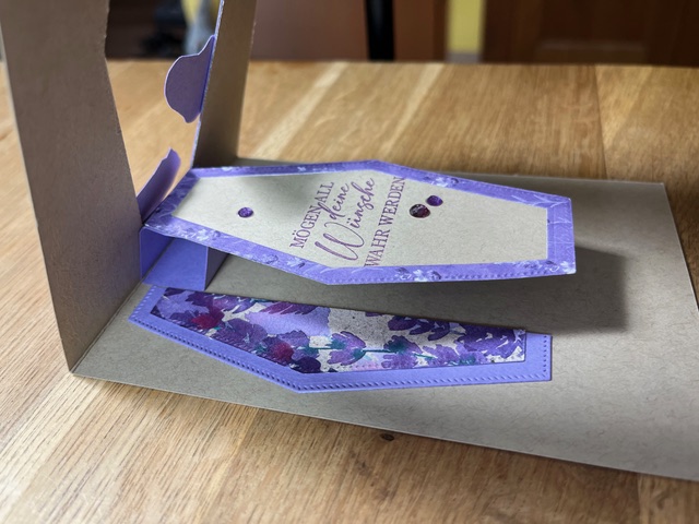 Grußkarte im Staffelei-Stil mit violettem Blumenmuster und Glitzerakzenten und der Nachricht „Mach was draus, 24. April.“