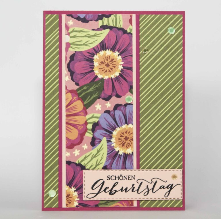 Eine Geburtstagskarte mit einem Blumendesign mit violetten und gelben Blumen und grünen Streifenmustern. Unten steht der Text „Schönen Geburtstag“, perfekt, um jemandem seinen besonderen Tag noch schöner zu machen. Mach was draus Mai 24.