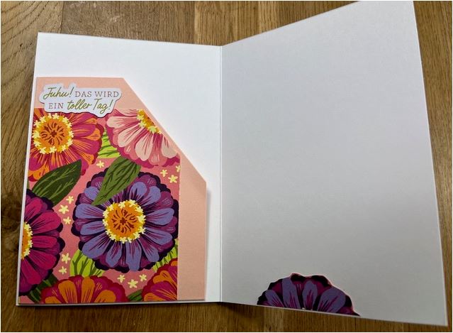 Eine offene Grußkarte mit bunten Blumenillustrationen auf der linken Seite und dem Text "Juhu! Das wird ein toller Tag!" auf rosa Hintergrund. Die rechte Seite ist leer und wartet auf Ihre persönliche Note. Sie lädt Sie ein, den Moment zu nutzen – Mach was draus Mai 24!