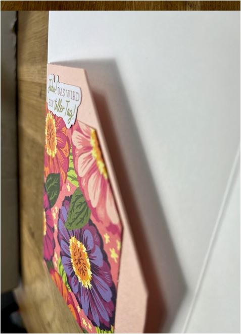 Eine bunte Grußkarte mit Blumenmotiven und dem deutschen Text „Ich das wird ein toller Tag! Mach was draus“ liegt auf einem Holztisch. Die Karte, perfekt für die Feierlichkeiten zum 24. Mai, steht auf einem weißen Hintergrund.