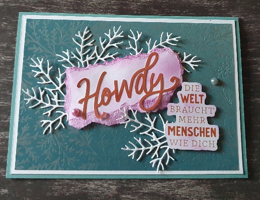 Eine Grußkarte mit „Howdy“ in großen Buchstaben auf einem rosa zerrissenen Stück Papier. Darunter steht auf Deutsch „Die Welt braucht mehr Menschen wie dich“. Weiße Zweigformen zieren die Karte. Perfekt für Mach was draus 24. Juni!