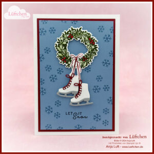 Eine Weihnachtskarte mit einem festlichen Kranz und einem Paar Schlittschuhe auf blauem Hintergrund mit Schneeflocken. Unter den Schlittschuhen steht der Text „LET IT Snow“ und deutet auf die Freude auf Weihnachten im Juli 2024 hin.