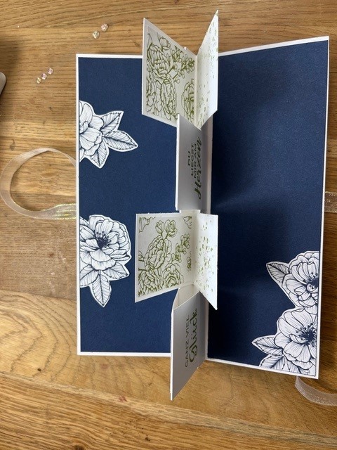 Eine handgemachte Pop-up-Karte mit Blumenmustern auf dunkelblauem Hintergrund, inspiriert von „Mach was draus“ vom 25. April, mit weißen Feldern, die sich öffnen lassen und im Inneren gestempelte Blumen und herzliche Botschaften zum Vorschein bringen.