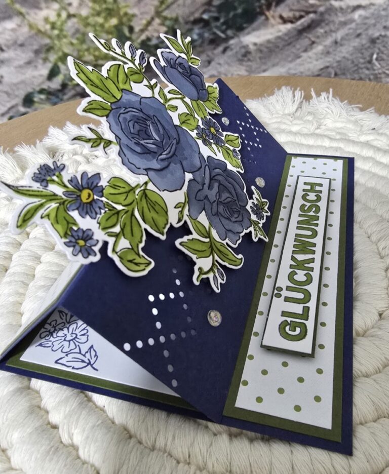 Eine handgemachte Pop-up-Karte mit blauen und grünen Blumenmustern und dem Schriftzug „GLÜCKWUNSCH“ auf der Vorderseite – perfekt, um „Mach was draus“ am 25. April auf kreative Weise zu feiern.