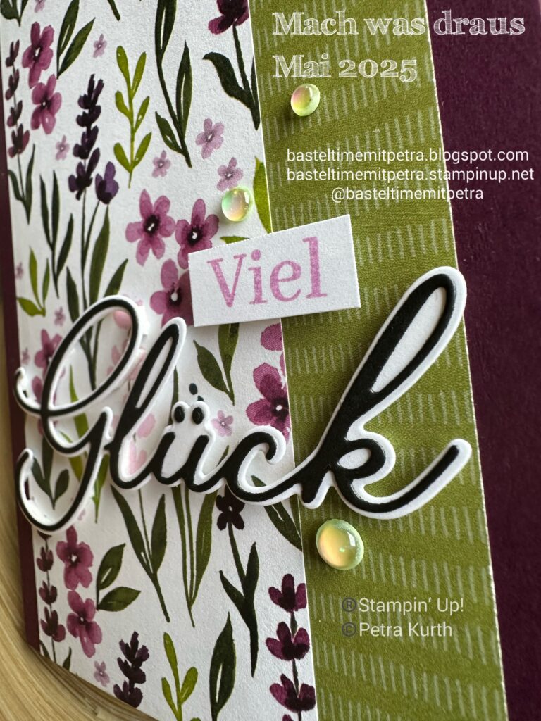 Handgefertigte Karte mit lila und grünen Blumenmustern, dem deutschen Text „Viel Glück“ und „Mach was draus Mai 25“ sowie transparenten Verzierungen. Blog- und Copyright-Informationen inklusive.
