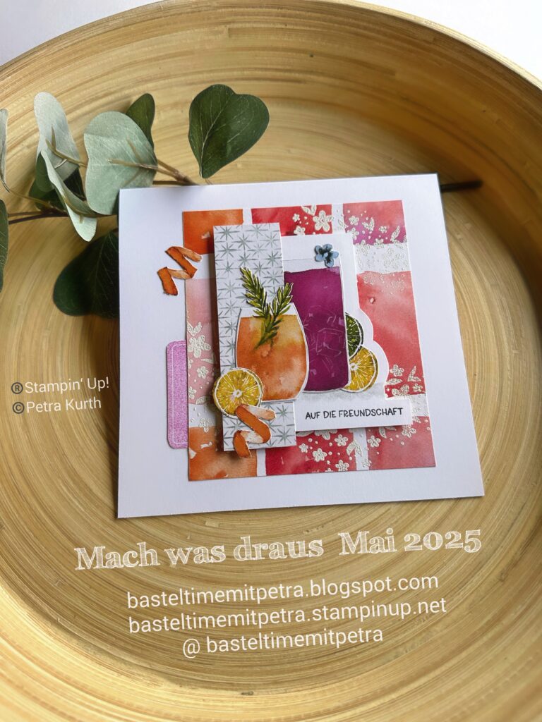 Eine handgefertigte Grußkarte mit Obst- und Blattmotiven auf rosa und orangefarbenem Hintergrund, präsentiert in einer Holzschale mit einem Zweig daneben. Textüberlagerungen heben Bastel-Websites hervor und bieten Inspiration für „Mach was draus Mai 25“.