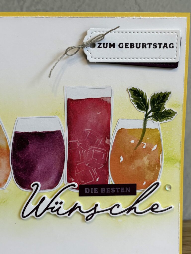 Eine Grußkarte mit Aquarellillustrationen von drei bunten Getränken, einer Blattgarnitur und deutschen Texten mit der Aufschrift „Zum Geburtstag“ und „Die besten Wünsche“. Perfekt für Mach war am 25. Mai!.