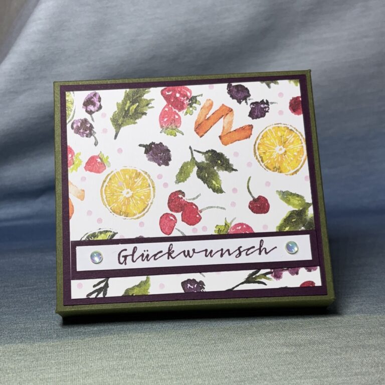 Für den 25. März wurde eine dekorative Karte mit Illustrationen von Früchten und Blättern erstellt, auf der das deutsche Wort „Glückwunsch“ auf einem Banner mit zwei kleinen Perlenverzierungen abgebildet ist.