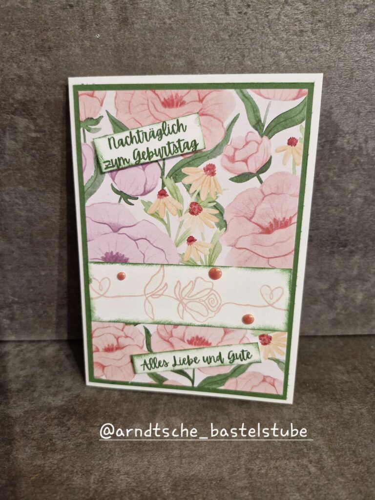 Eine handgefertigte florale Geburtstagskarte von Mach was draus 25. Juni zeigt den deutschen Text "Nachträglich zum Geburtstag" und "Alles Liebe und Gute" auf einem rosa-grünen Hintergrund, aufrecht stehend auf einer braunen Oberfläche.