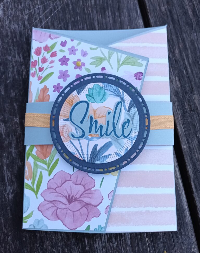 Eine handgefertigte Blumenkarte von Mach wurde am 25. Juni mit einer blau-goldenen Banderole und dem Schriftzug "Smile" in der Mitte auf eine Holzunterlage gelegt.