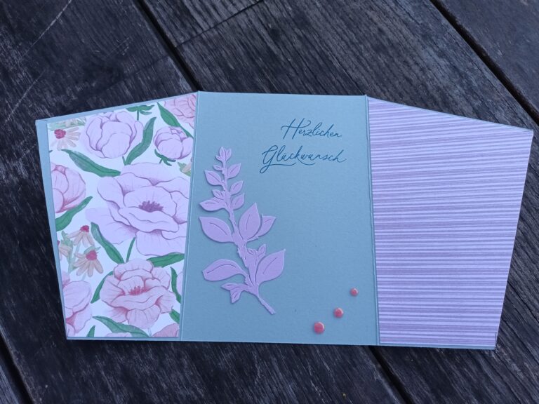 Eine handgefertigte Grußkarte, die von Mach inspiriert ist, wurde am 25. Juni draus gemacht. Sie besteht aus drei Feldern: links ein Blumenmuster, in der Mitte ein hellblaues Blattmuster mit deutschem Text und rechts ein gestreiftes Muster, alles auf einer Holzoberfläche.
