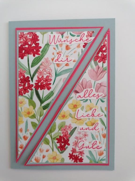 Eine Grußkarte von Mach was draus 25. Juni zeigt rote und gelbe Blumen und den deutschen Text "Wünsche dir alles Liebe und Gute" auf einem weißen und hellblauen Hintergrund.