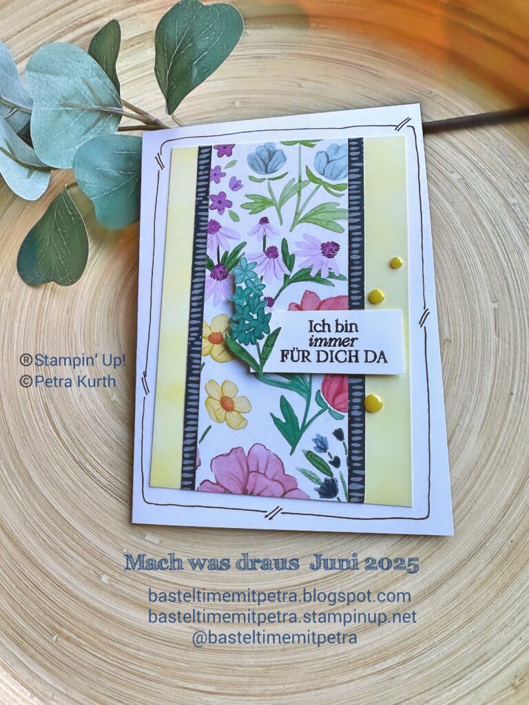 Eine handgefertigte Blumengrußkarte mit deutschem Text, gelben Akzenten und Blattverzierungen von Mach wurde am 25. Juni auf einer Holzfläche mit Eukalyptusblättern daneben ausgelegt.