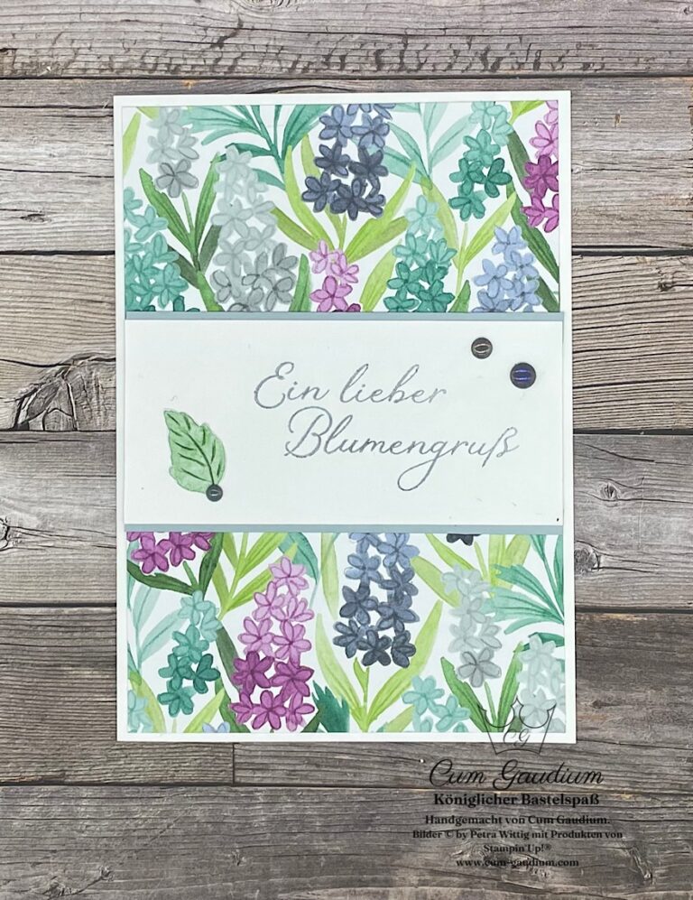 Eine Grußkarte mit Blumen im Aquarellstil in Lila, Rosa und Blau und dem deutschen Text "Ein lieber Blumengruß" in der Mitte - perfekt für Ihr Projekt Mach was draus 25. Juni.