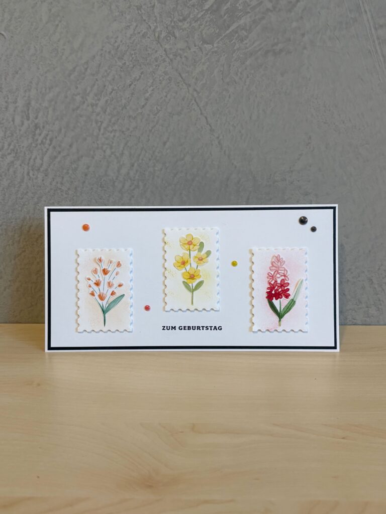 Eine rechteckige Grußkarte mit drei floralen Illustrationen und dem deutschen Text "ZUM GEBURTSTAG" auf einer hölzernen Oberfläche, die als Teil von Mach was draus 25. Juni vorgestellt wurde.