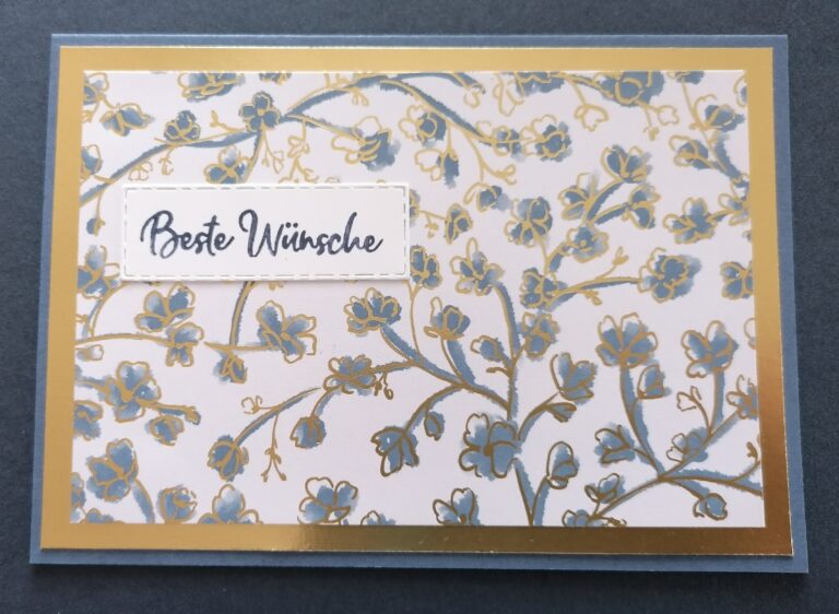 Eine Grußkarte mit einem blau-goldenen Blumenmuster und einem weißen Etikett in der Mitte, auf dem in Schreibschrift "Beste Wünsche" steht, perfekt für Mach was draus 25. Juli-Feiern.