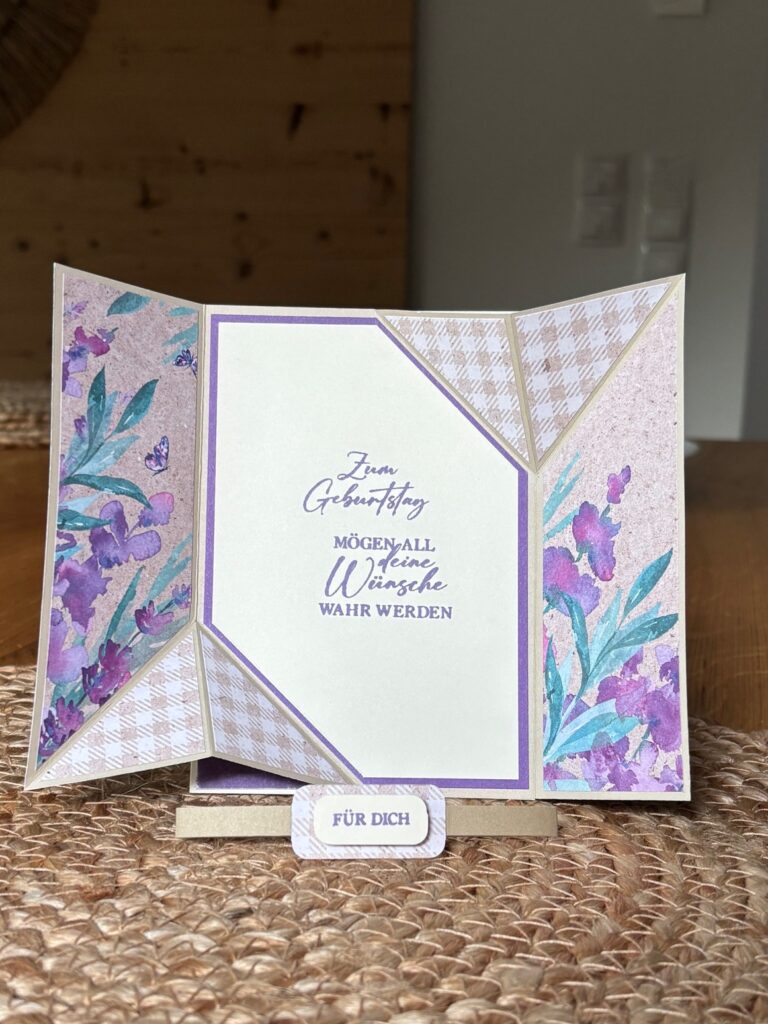 Eine handgefertigte Geburtstagskarte mit geometrischen Feldern, floralen Motiven und deutschem Text, die aufrecht auf einem Tisch steht. Auf einem kleinen Etikett auf der Vorderseite steht "Für dich". Die Karte wurde für Mach was draus am 25. August entworfen und ist eine charmante Note für jede Feier.