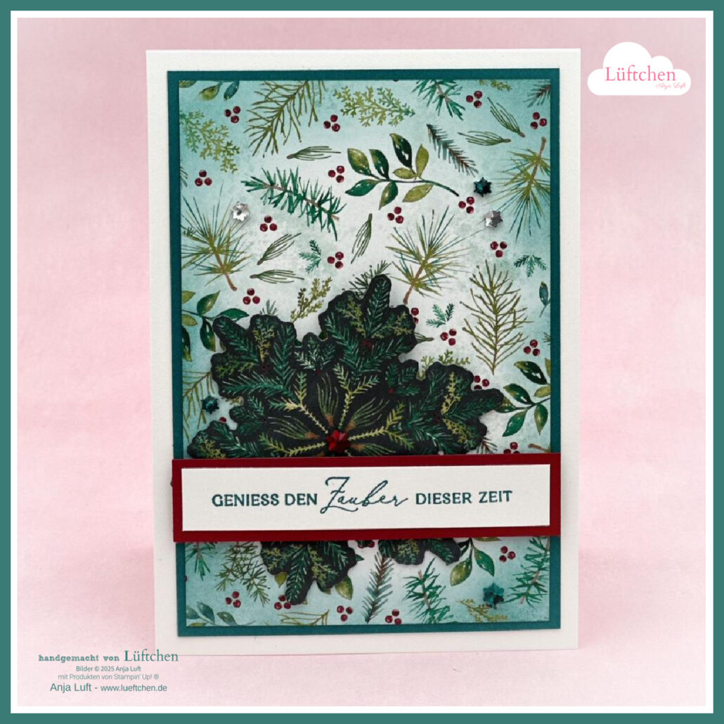 Eine handgefertigte Weihnachtskarte mit grünem und rotem Tannenmotiv, einer mehrschichtigen Stechpalmenverzierung und dem deutschen Text "GENIESS DEN ZAUBER DIESER ZEIT" auf einem weißen Banner - perfekt für Mach was draus 25. Oktober.