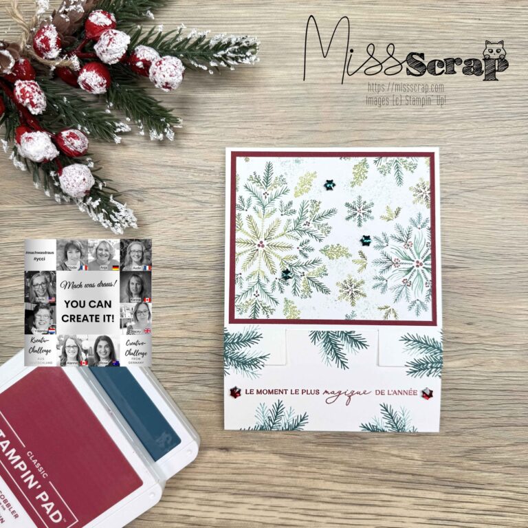 Eine handgefertigte Weihnachtskarte mit Tannen- und Beerenmotiven liegt auf einem Holztisch neben roten und blauen Stempelkissen, einer kleinen Karte, gefrostetem Kunstbeeren-Dekor und einem "Mach was draus 25. Oktober"-Anhänger für eine festliche, kreative Note.