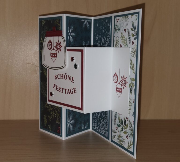 Eine handgefertigte Feiertagskarte von Mach was draus 25. Oktober mit dem deutschen Text SCHÖNE FESTAGE", verziert mit Ornamenten und botanisch gemustertem Papier, steht offen auf einer Holzfläche.