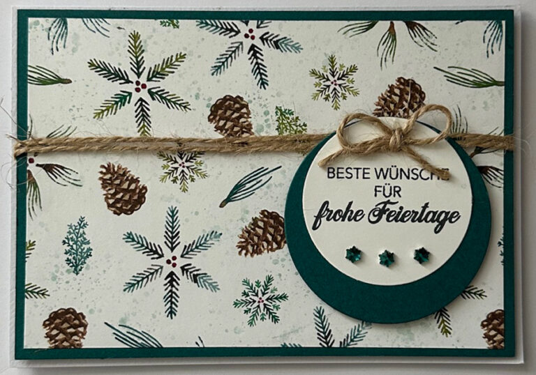 Eine Weihnachtskarte von Mach was draus 25. Oktober zeigt Tannenzapfen und -zweige, eine Schleife aus Garn und ein rundes Schild mit der Aufschrift "Beste Wünsche für frohe Feiertage", das mit drei grünen Edelsteinen unterhalb des Textes verziert ist.