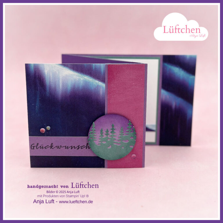Eine handgefertigte Grußkarte von "Mach was draus Oktober 25" mit einem lila und blauen Aurora-Motiv, dem deutschen Text "Glückwunsch" und einer kreisförmigen Waldsilhouette als Verzierung.