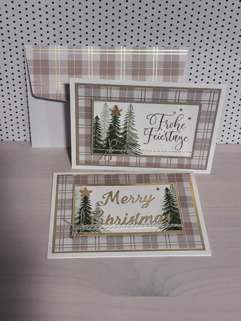 Zwei karierte Weihnachtskarten mit Baummotiven und goldenem Text "Frohe Feiertage" und "Merry Christmas" werden auf einer hellen Holzoberfläche mit einem passenden Umschlag präsentiert - perfekt für Mach was draus 25. Dezember-Feiern.