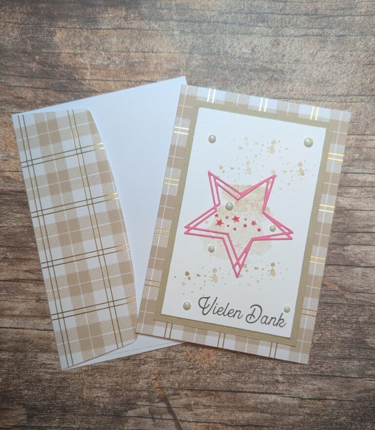 Eine Danksagungskarte mit karierter Umrandung und passendem Umschlag, die ein rosafarbenes Sternmotiv und die deutsche Phrase "Vielen Dank" enthält, inspiriert von Mach was draus 25. Dezember, dargestellt auf einer Holzoberfläche.