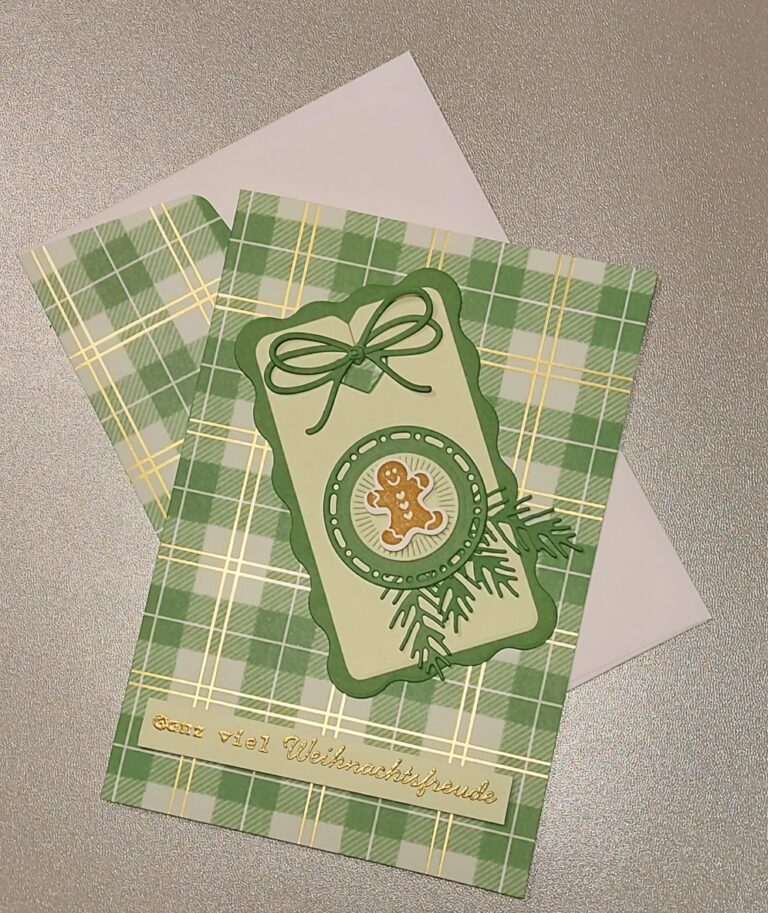 Eine grün karierte Weihnachtskarte mit einem Lebkuchenmännchen, Tannenzweigen und dem Text "Sehr viel Weihnachtsfreude" auf der Unterseite, perfekt für Mach was draus 25. Dezember, auf einer silbernen Oberfläche mit einem Umschlag.