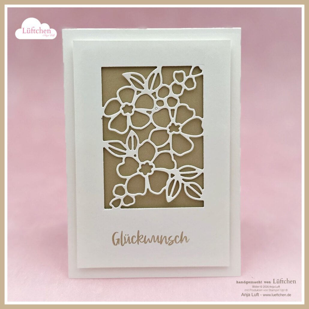 Eine weiße Grußkarte mit einem floralen Ausschnitt und dem Wort "Glückwunsch" darunter, exklusiv online ab 26. Januar, vor einem zartrosa Hintergrund.