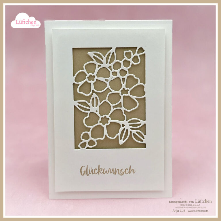 Eine weiße Grußkarte mit einem floralen Ausschnitt und dem Wort "Glückwunsch" darunter, exklusiv online ab 26. Januar, vor einem zartrosa Hintergrund.