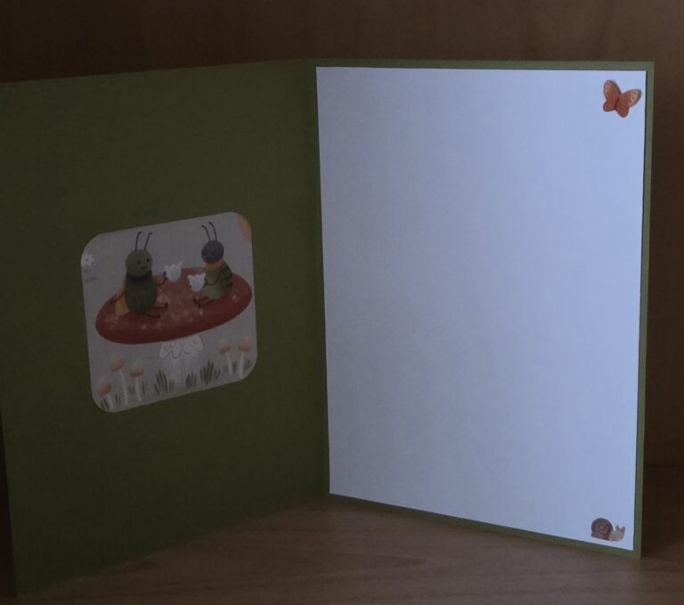 Eine offene Grußkarte mit zwei Cartoon-Insekten auf einem Pilz auf der linken Seite und einer leeren weißen Fläche mit einem Schmetterling, einer Schnecke und "Mach was draus Februar 26" auf der rechten Seite.