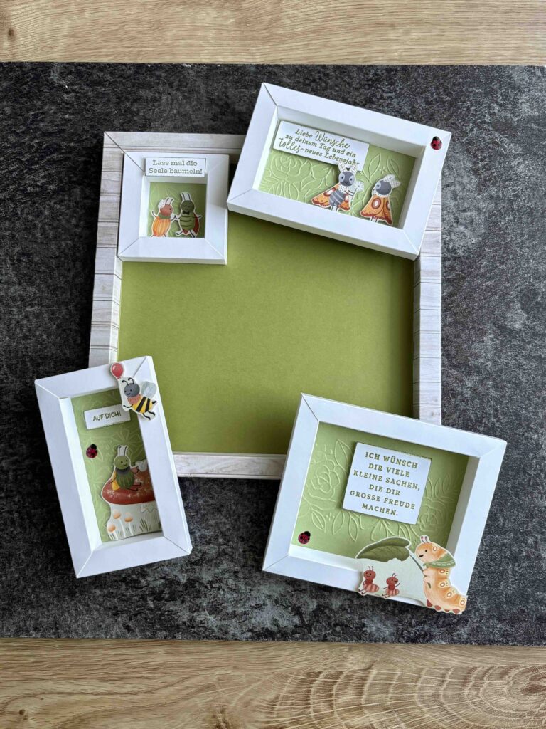 Vier weiß umrandete Bilderrahmen mit deutschen Texten und Tierillustrationen, Teil des Projekts "Mach was draus Februar 26", sind auf einer Holz- und Schieferfläche angeordnet; drei zeigen Kunst, einer bleibt leer mit einem grünen Hintergrund.