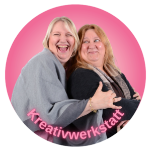 Anja und Petra, die sich lächelnd umarmen, vor einem rosafarbenen Hintergrund. Kreativwerkstatt. Workshop