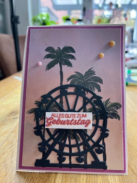 Eine handgefertigte Geburtstagskarte, die von Mach inspiriert wurde, wurde am 26. März draus, mit einem Riesenradausschnitt, Palmen im Hintergrund und dem deutschen Text "Alles Gute zum Geburtstag" auf der Vorderseite.