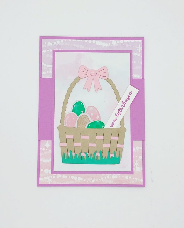 Eine handgefertigte Osterkarte mit einem Korb mit pastellfarbenen Eiern, einer rosa Schleife und einem "von Ostern"-Anhänger auf einem lila-rosa Hintergrund - perfekt, um die Freude mit der Mach was draus"-Gemeinschaft zu teilen.