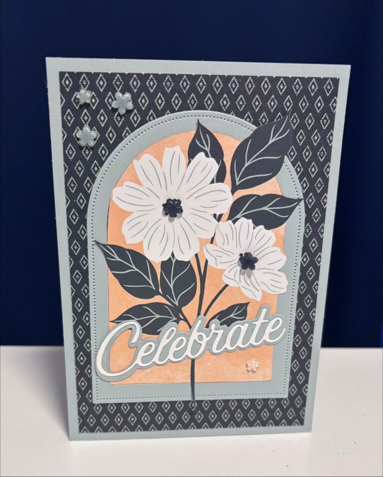 Grußkarte mit "Celebrate"-Text, mit weißen Blumen mit dunklen Zentren auf einem pfirsichfarbenen Hintergrund, umrandet von einem schwarzen und weißen geometrischen Muster - perfekt für Mach was draus 26. April Momente.