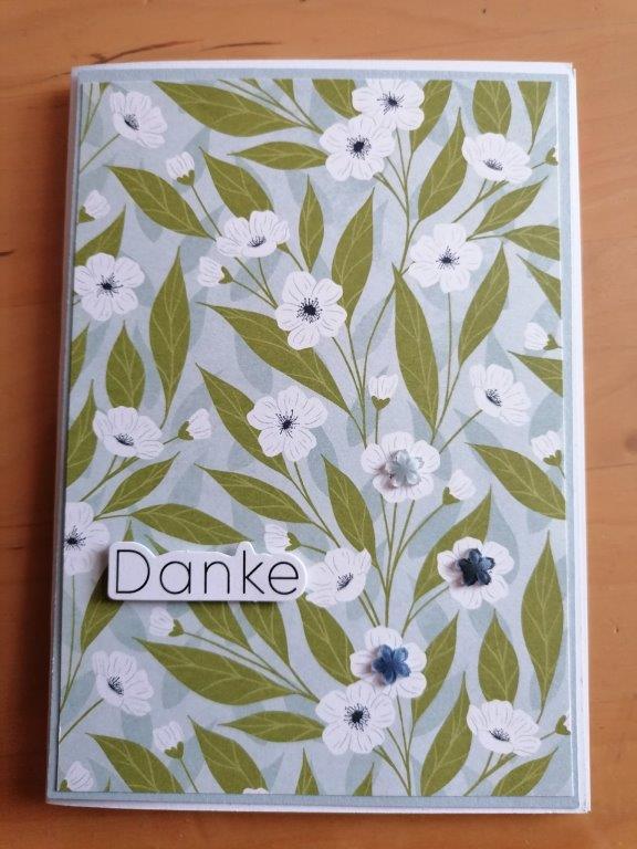 Eine Karte mit einem floralen Muster aus weißen Blüten und grünen Blättern auf hellblauem Hintergrund und dem Wort "Danke" in schwarzen Buchstaben auf einem weißen Rechteck - ein schönes Projekt für Mach war draus 26. April.