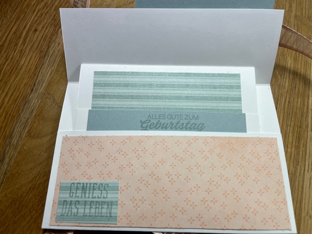 Eine handgefertigte Geburtstagskarte mit Umschlägen und dekorativem Papier mit dem deutschen Text "Alles Gute zum Geburtstag" und "Genieß das Leben", inspiriert von Mach, wurde am 26. April auf einer Holzfläche ausgestellt.