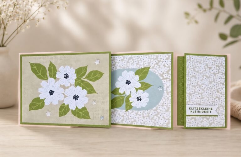 Eine handgefertigte dreifaltige Karte mit weißen Blumen und grünen Blättern auf zartgrünem Hintergrund, die für Mach erstellt wurde, wurde am 26. April draus, mit einem Blumenmuster und einem kleinen Etikett mit der Aufschrift "KLITZEKLEINE KLEINIGKEIT".