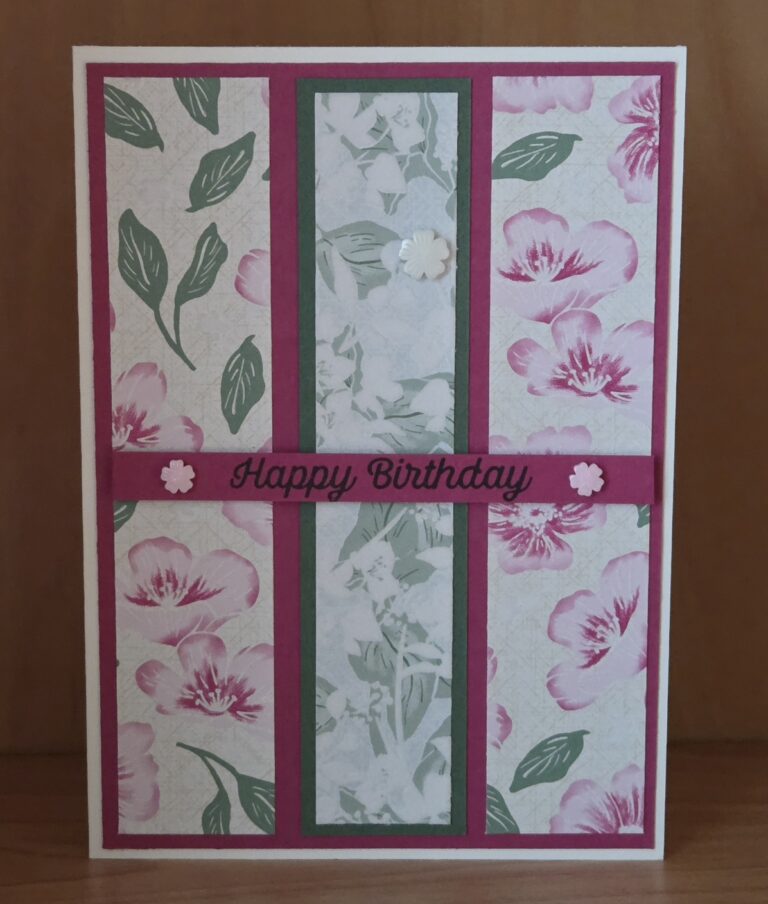 Handgefertigte Geburtstagskarte mit rosa Blumenmustern, grünen Blättern und der Aufschrift „Happy Birthday“ auf einem rosa Streifen, verziert mit kleinen weißen Blumen. Inspiriert von „Mach was draus“ vom 26. Mai.