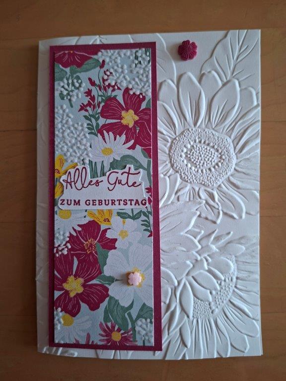 Eine handgefertigte Geburtstagskarte, inspiriert von Mach, vom 26. Mai, mit geprägten weißen Sonnenblumen und einem Blumenmuster. Der deutsche Text lautet: „Alles Gute zum Geburtstag.“.