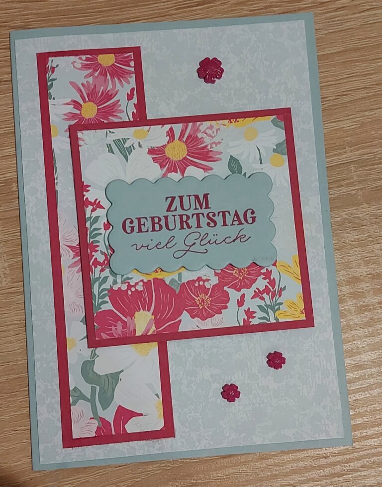 Eine Geburtstagskarte mit Blumenmotiv und dem deutschen Text „Zum Geburtstag viel Glück“ auf hellblauem Hintergrund, verziert mit rosa Blumen und einem roten Rand. Teil der Kollektion „Mach was draus – Mai 26“.