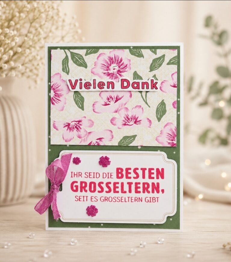 Eine dekorative Dankeskarte mit Blumenmotiven und dem deutschen Text „Mach was draus – 26. Mai“, die aufrecht auf einem Tisch steht, im Hintergrund sind verschwommene Pflanzen zu sehen.