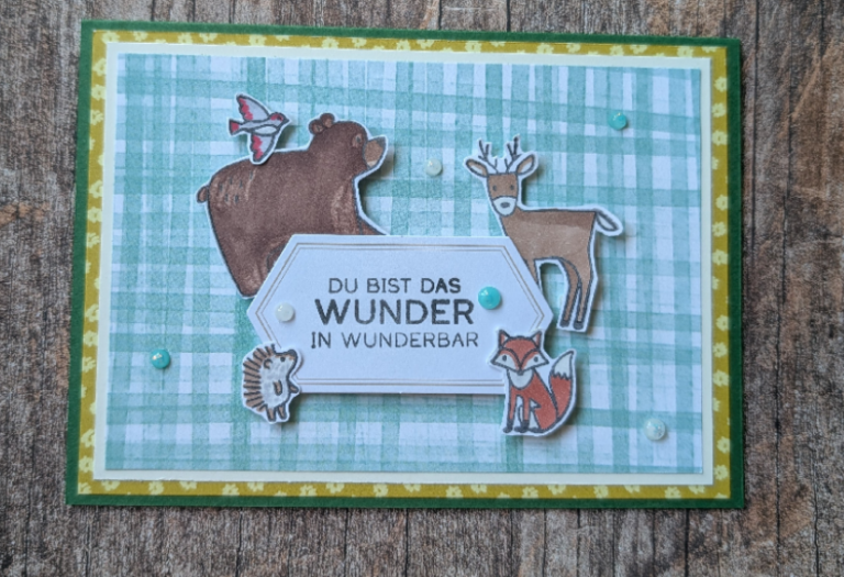 Eine handgefertigte Grußkarte für Mach, datiert auf den 26. Juni, zeigt Ausschnitte eines Bären, eines Rehs, eines Fuchses, eines Igels und eines Vogels, die ein Schild mit der Aufschrift „Du bist das Wunder in wunderbar“ auf grünem Karomuster umrahmen.
