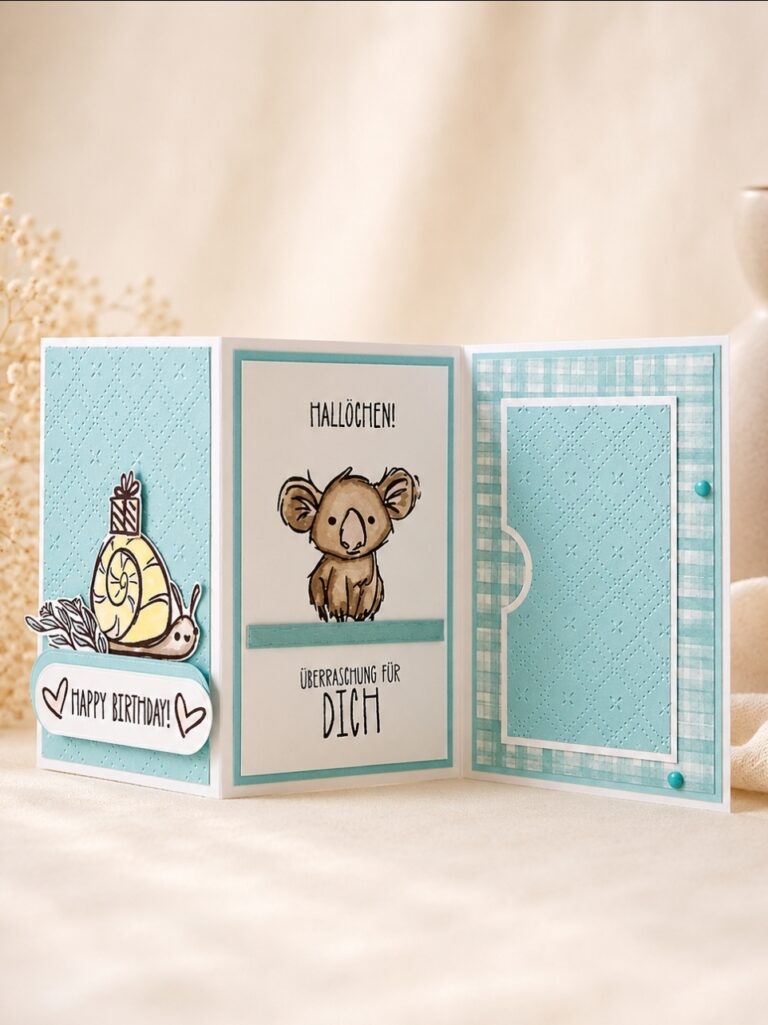Eine handgefertigte Dreifachklappkarte für Mach wurde am 26. Juni gestaltet; darauf waren links eine Schnecke mit der Aufschrift „Happy Birthday!“, in der Mitte ein Koala mit „Hallöchen!“ und „Überraschung für dich“ sowie rechts ein blau gemustertes Feld zu sehen.